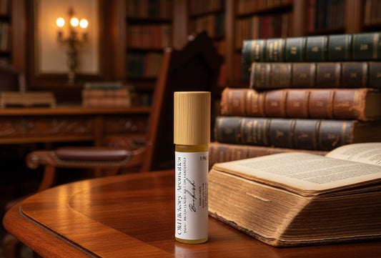 Small rollerball bottle with wooden cap and white label of Old Hickory Aromatics Bookish Roll On Fragrance on a rosewood desk surrounded by leather bound books and a personal library.