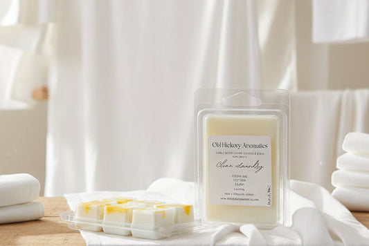 Two six cell clamshells of Old Hickory Aromatics Clean Laundry Wax Melts on a laundry room counter with clean white sheets on the counter and hanging to dry in the background. 